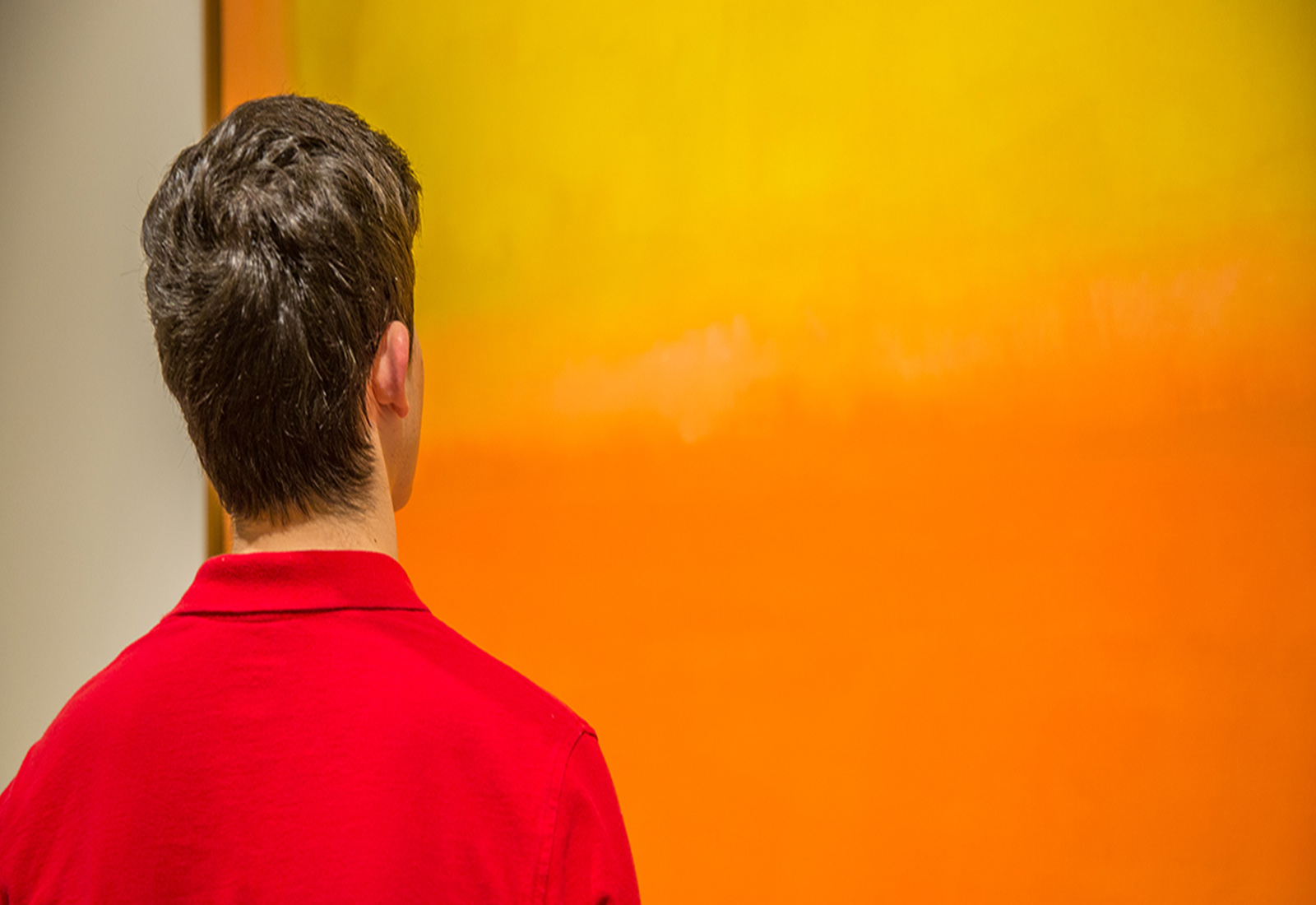 Man looking at orange and yellow painting